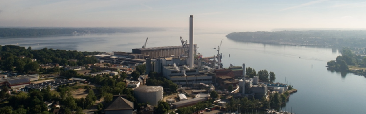 Blick aus der Vogelperspektive auf das Kraftwerk Flensburg mit Schornstein, Hafenanlagen und der Flensburger Förde